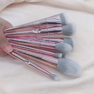 Detail view of 7 rose gold makeup brushes with soft grey-white bristles on beige fabric