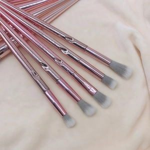 Close-up of five rose gold makeup brushes with synthetic bristles on beige fabric