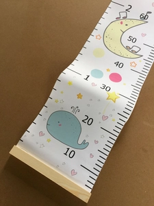 Detail of canvas height chart featuring cartoon whale moon pattern and wooden hangers