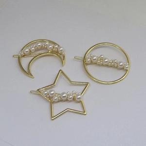 Close-up of three gold-tone hair clips with pearls in moon, star, and circle shapes