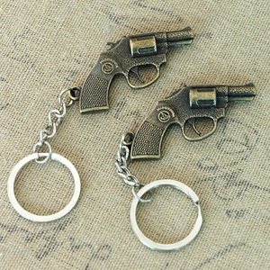 Detail of two vintage bronze revolver-shaped metal keychains on a textured background