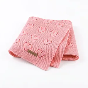 Pink knitted baby blanket with hollow heart patterns and premium leather label detail