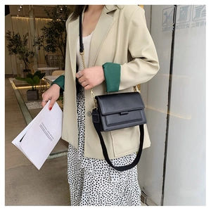 Chic black crossbody bag with wide fabric strap and gold hardware on a stylish model