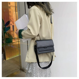 Detail showing classic black crossbody bag with contrast stitching and metal chain strap