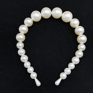 Macro view of a white faux pearl headband with graduated beads on black velvet