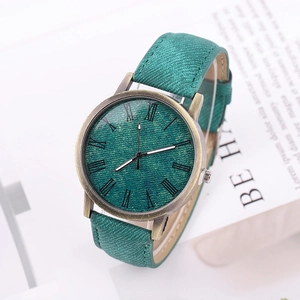 Retro bronze watch with green denim texture strap and Roman numeral dial on a desk