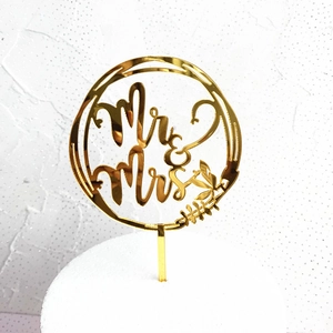 Close-up of golden Mr & Mrs cake topper with round frame and leaf motif on white cake
