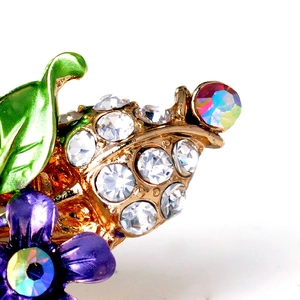 Macro detail of hand-painted purple flower hair clip with sparkling crystals on gold metal