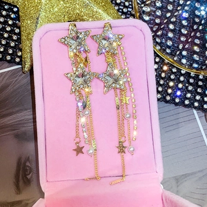 Macro view of gold star earrings with rhinestone fringe and pearls in a pink jewelry box