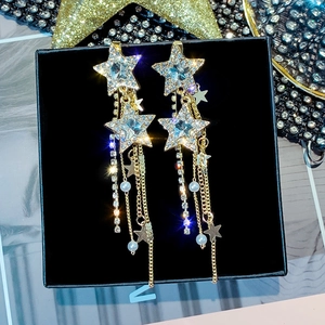 Macro detail of gold star earrings with sparkling rhinestones and pearl tassels