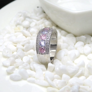 Detail of silver wedding ring with pink and purple zirconias on white pebbles