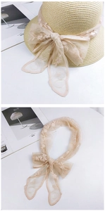 Close-up of beige lace scarf with embroidered floral edges and wavy trim on straw hat