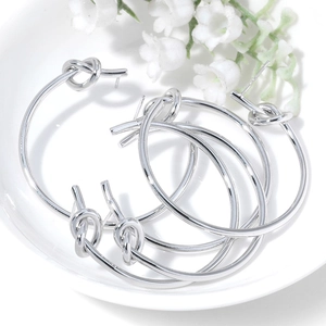 Three pairs of silver knotted hoop earrings shown on a white plate with floral accents