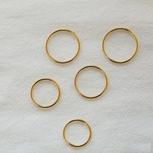 Detailed top view of five minimalist thin gold bands on a white textured fabric background
