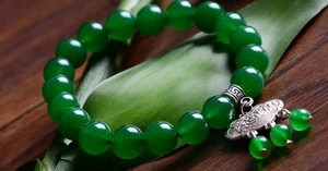 Detail of beaded bracelet with green jade-like beads and silver longevity lock pendant