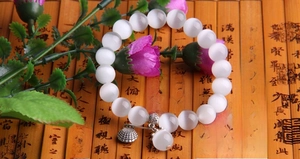 Detailed macro of a white cat eye stone bead bracelet with metal charms on bamboo
