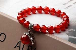 Detailed view of a red bead bracelet featuring a silver apple and leaf charm pendant