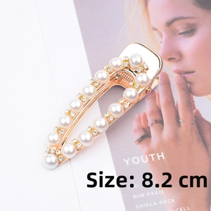 Detail of an 8.2cm gold hair clip with white pearls and rhinestones on a magazine background