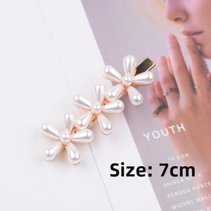 Detail view of 7cm long golden metal hair clip with three white pearl flower designs