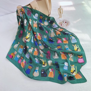 Detailed view of a green silk scarf with cat prints draped on a beige handbag