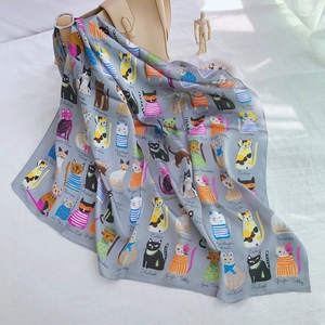 Detail of silk scarf with cat illustrations draped over a beige handbag in lifestyle setting