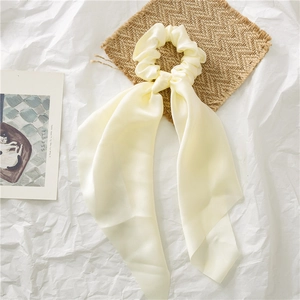 Close-up van een crème satijnen scrunchie met lange linten op decoratieve achtergrond