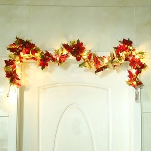 Red and gold Christmas poinsettia garland with warm LED lights on a white door