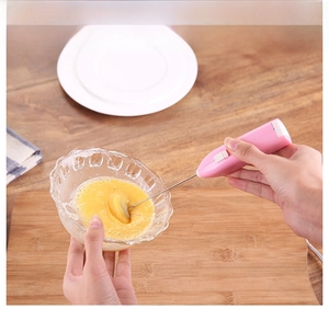 Action shot of pink electric hand mixer whisking eggs in a glass bowl on kitchen counter