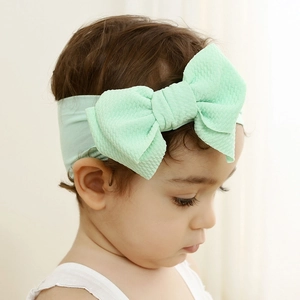 Close-up of mint green nylon baby headband with textured fabric and oversized knot bow