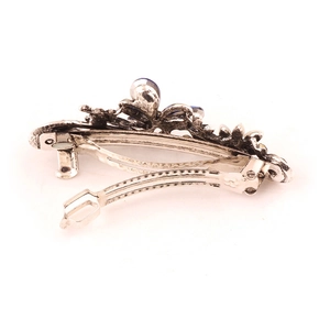 Retro silver hair clip with blue rhinestones and floral embossed texture on white background