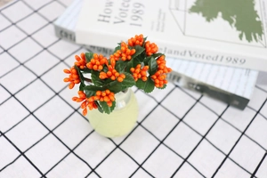 Detail of orange artificial berries with green leaves in a small green ceramic vase