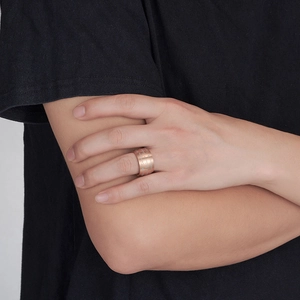 Close-up of a wide rose gold band ring with artistic letter engraving on a model's hand