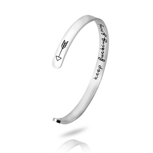 Macro detail of silver stainless steel cuff with engraved keep fucking going text