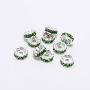 Macro shot of silver metal rondelle beads with inlaid green rhinestones on white background