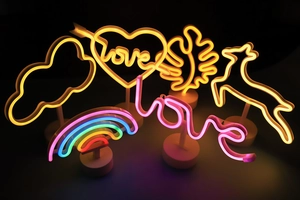 Variety of LED neon light shapes including rainbow, heart, and leaves on round white bases
