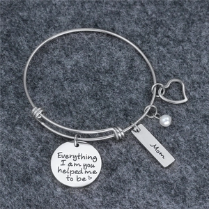 Close-up of engraved silver bangle with Mom tag, heart charm and pearl on grey felt