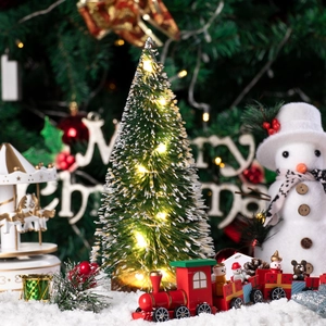 Mini cedar Christmas tree with LED lights, wooden toy train, and snowman on snow
