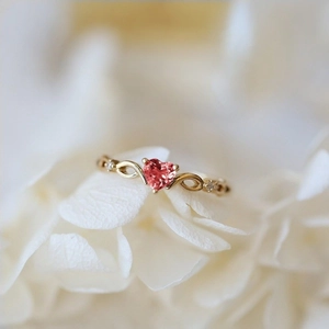 Elegant gold heart ring with pink gemstone and zircon on white petals background