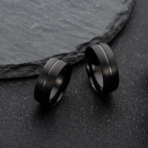 Macro detail of 8mm matte black stainless steel rings with center groove on dark rock