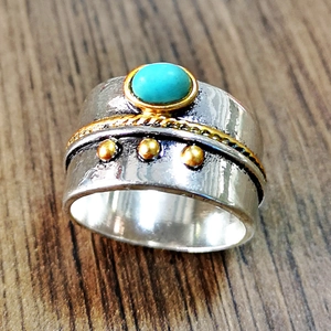 Macro shot of oval turquoise setting with golden twisted accents on vintage silver band