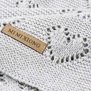 Knitted baby blanket with hollow heart pattern in soft light grey featuring leather logo tag