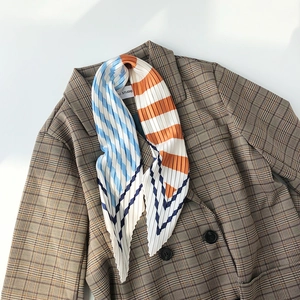 Detail of pleated silk scarf with blue and orange geometric stripes on a brown blazer