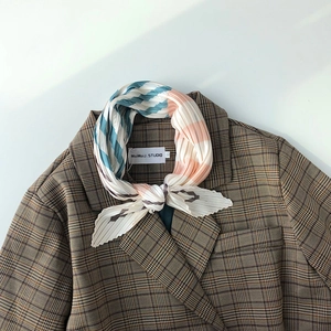 Close-up of pleated silk scarf with colorful wave pattern tied on a brown plaid blazer