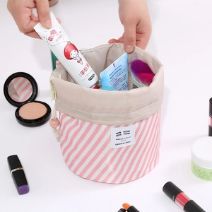 Pink striped drawstring Oxford cloth travel makeup bag being packed with cosmetics