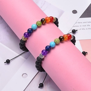 Dettaglio di braccialetti in pietra lavica chakra con ciondoli su base rosa