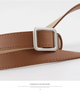 Detail of square silver metal buckle and brown leather strap with yellow stitching