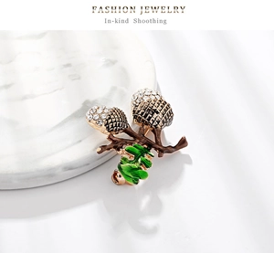 Detailed macro view of rhinestone hazelnut brooch with green enamel leaf on marble base