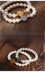 Detailed view of pearl bracelets with gold and silver heart pendants on wood surface