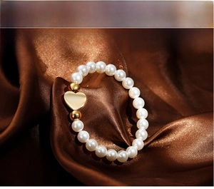 Close-up of elegant pearl bracelet with golden heart charm on dark brown satin background