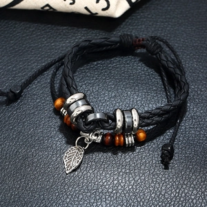 Macro shot of multi-layer leather bracelet featuring a silver leaf pendant and wooden beads